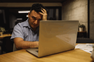 Homme en perte de confiance chez les dirigeants, se tenant la tête devant son ordinateur, illustrant le besoin d’un accompagnement par le mentorat.
